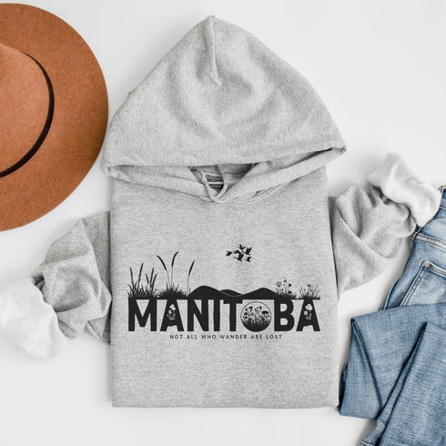 Featuring a prairie landscape, the design showcases wildflowers and prairie grasses blooming from the letters "Manitoba," artfully integrated into the scene.